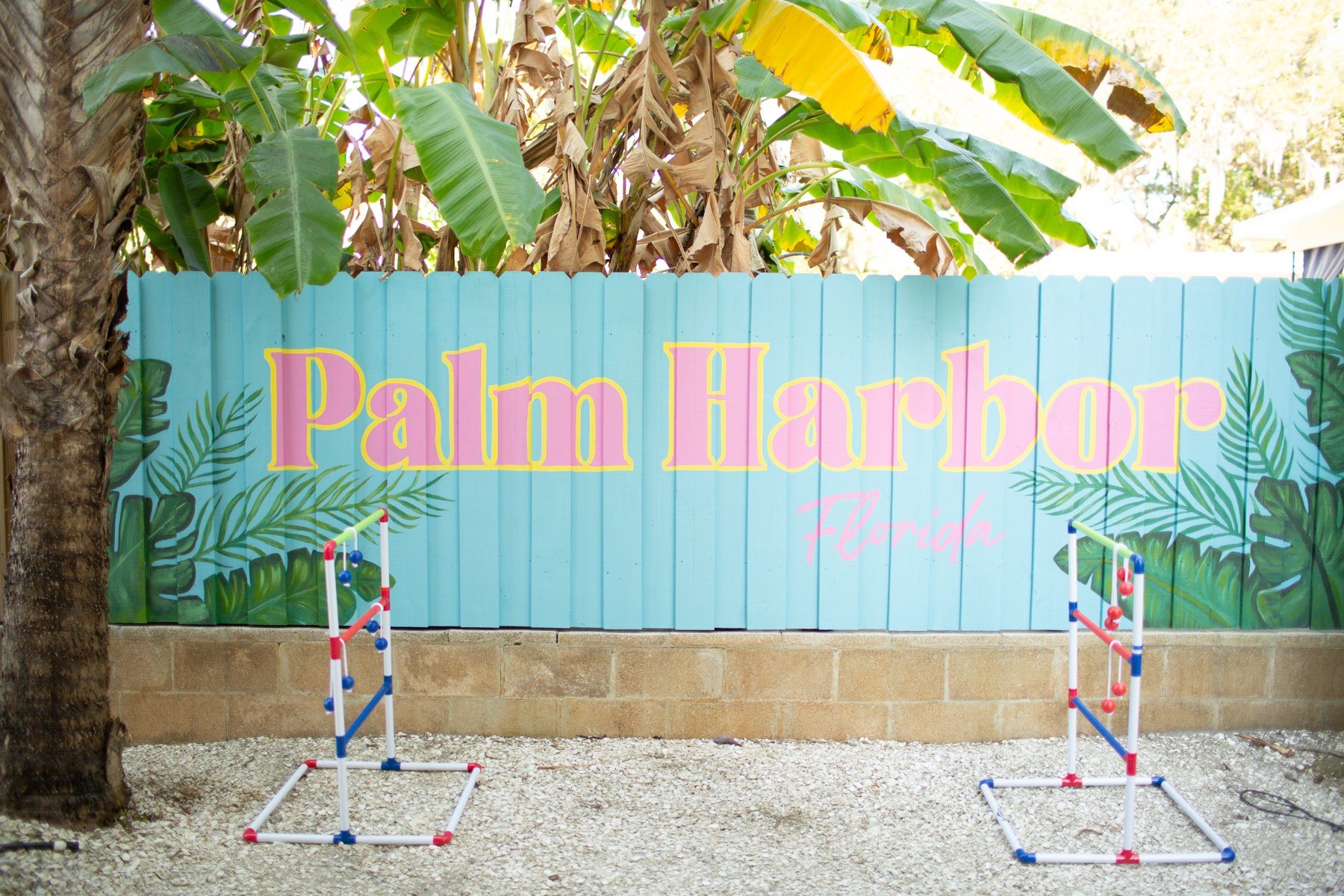 Hand-painted Palm Harbor Florida mural on the backyard fence with two ladder toss sets