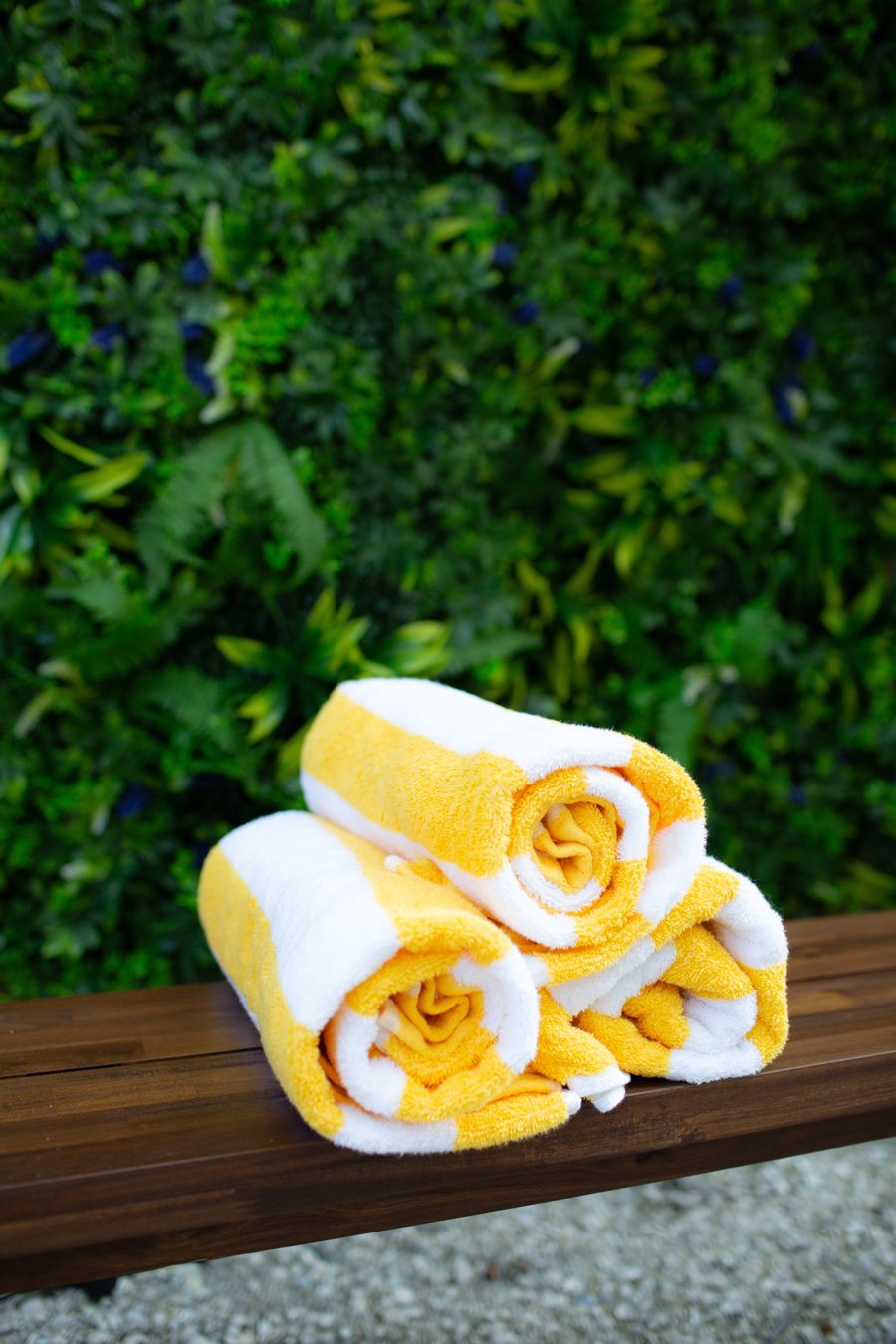 Rolled yellow and white striped beach towels on a wood bench
