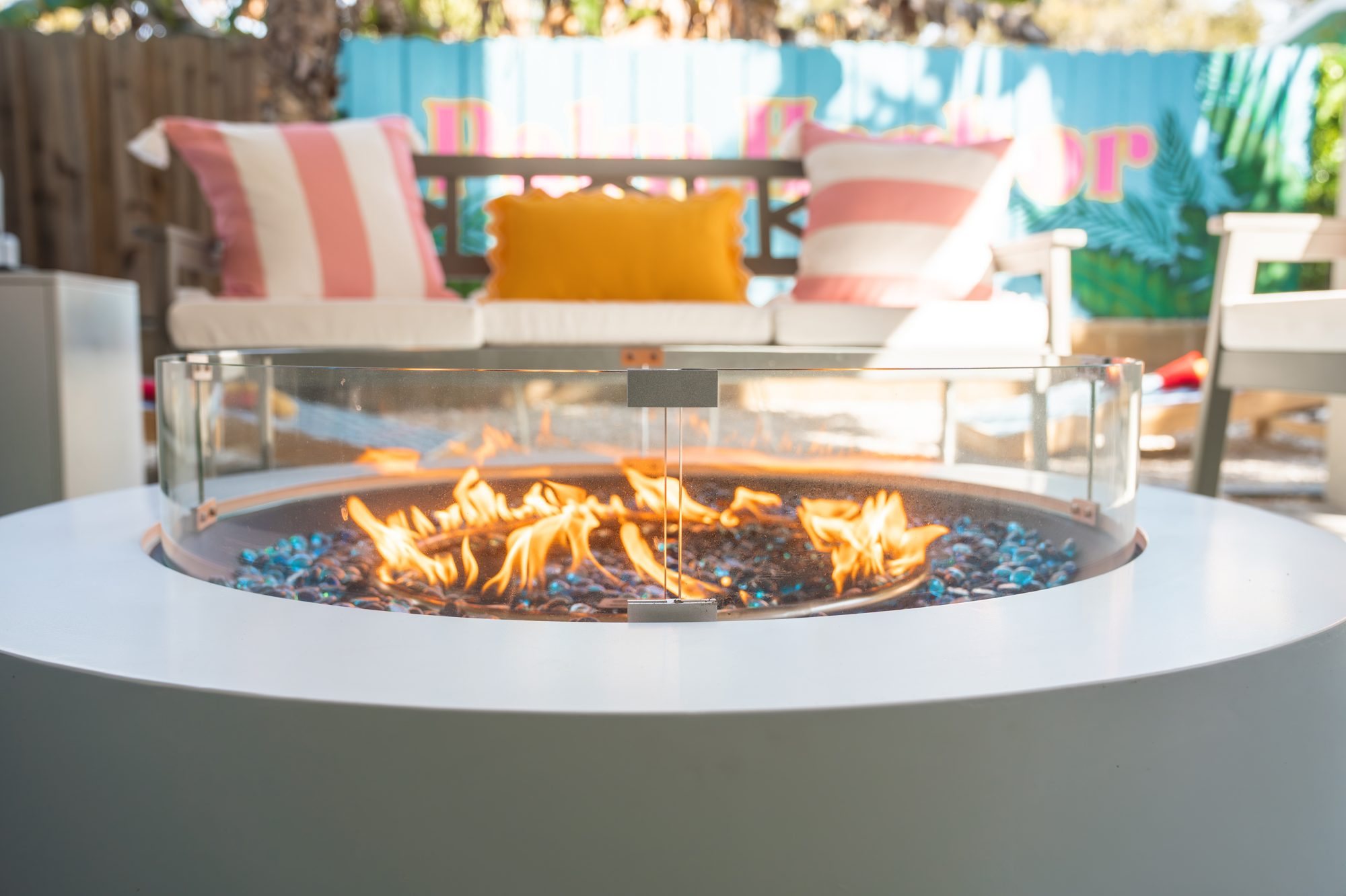 Gas fire pit with glass guard in front of the patio sofa and Palm Harbor mural