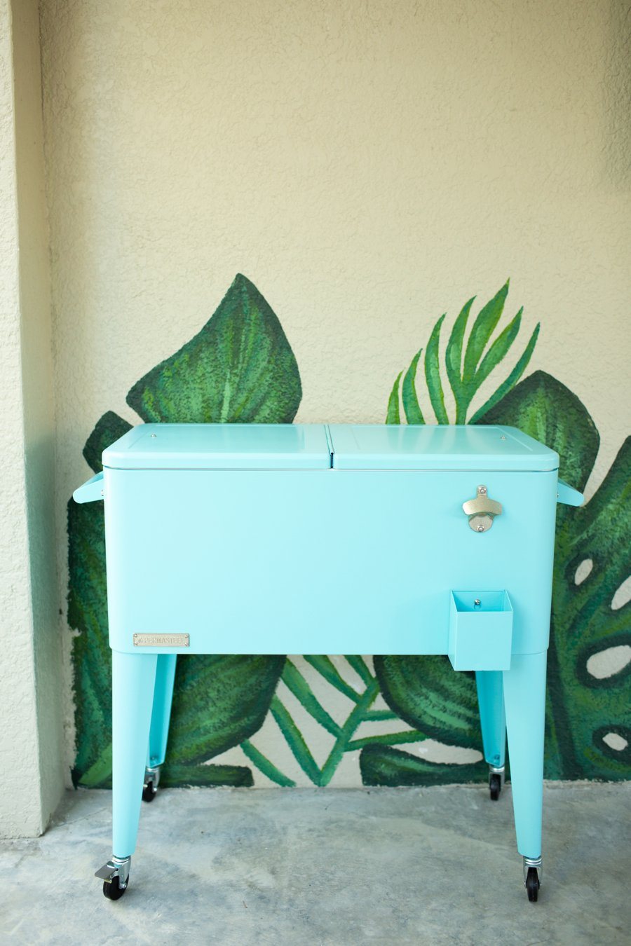 Aqua rolling cooler in front of a painted tropical leaf mural