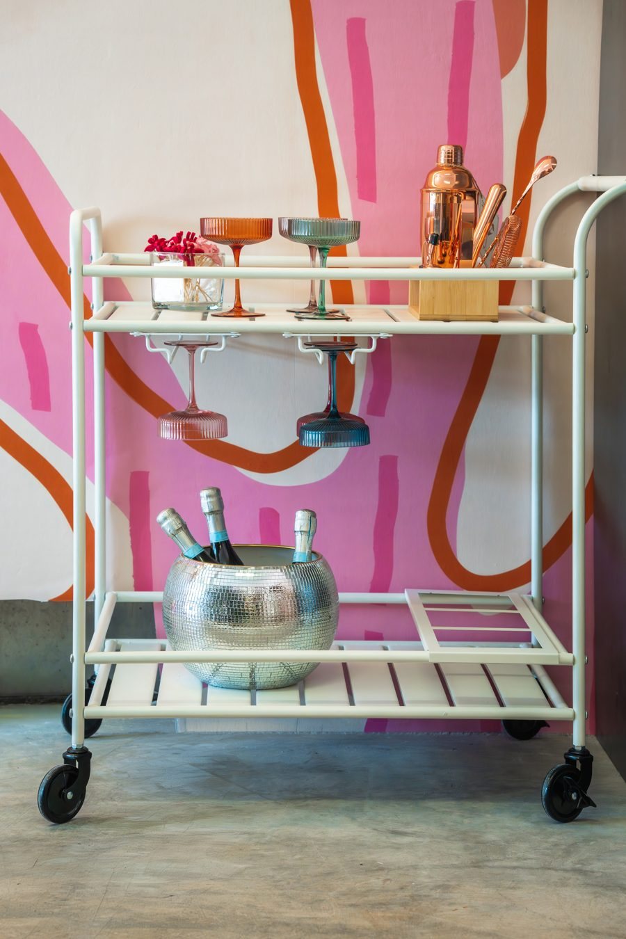Bar cart with colorful coupe glasses and a disco ice bucket