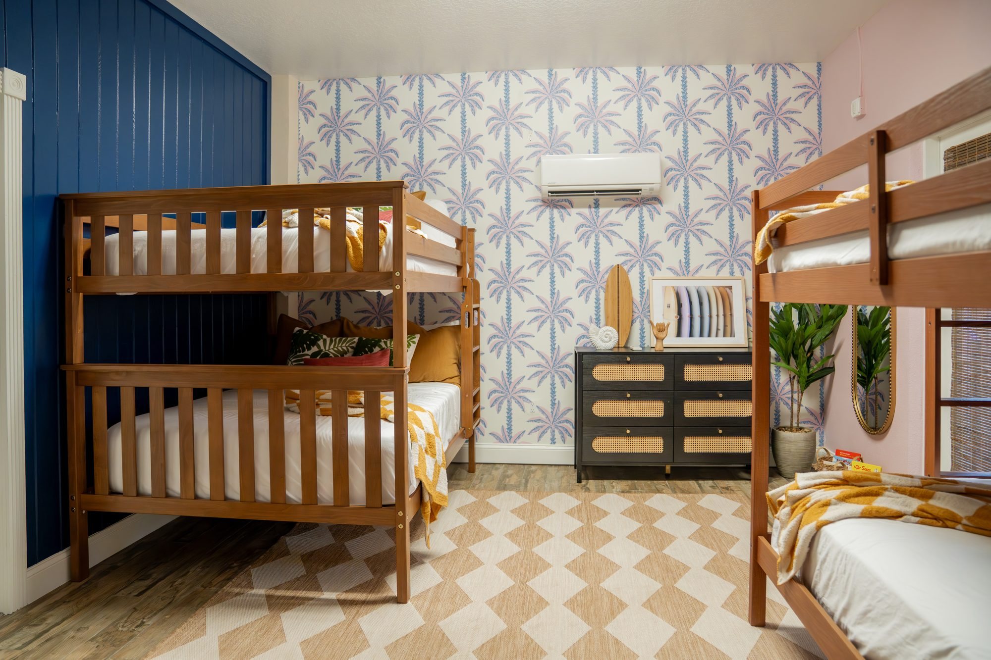 Bunk room with two wooden bunk beds, palm tree wallpaper and a surf-themed dresser