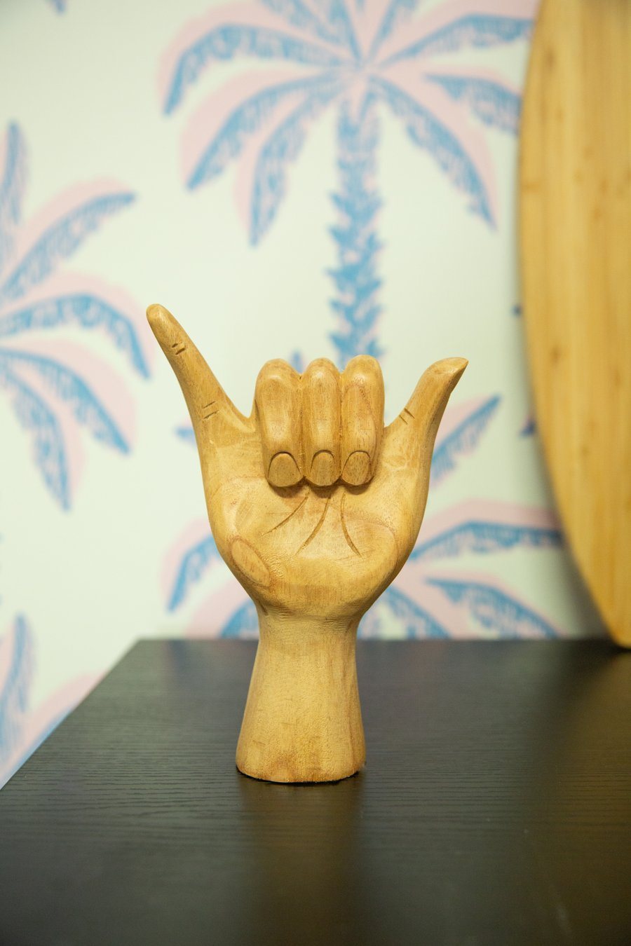 Carved wooden shaka hand in front of palm tree wallpaper